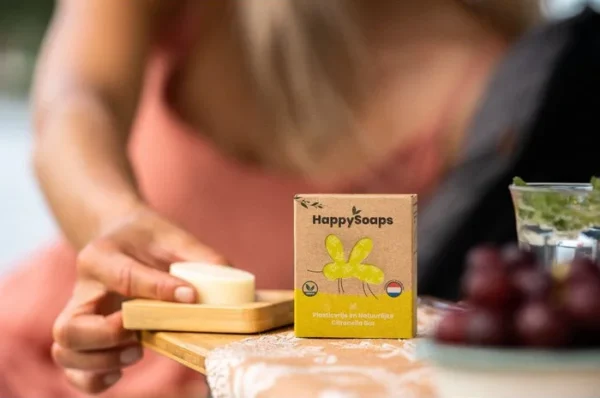 Produktbild Happy Soaps Mückenschutz. Im Hintergrund sieht man verschwommen ein Frau, welche die ausgepackte Happy Soaps Bar in die Hand nimmt.